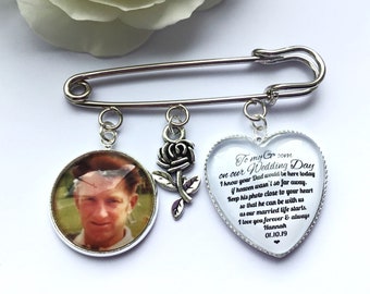 May include: A silver-toned safety pin brooch featuring three dangling charms: a circular pendant with a man's photograph, a small rose charm, and a heart-shaped pendant with black text that reads: To my Groom on our Wedding Day. I know your Dad would be here today if heaven wasn't so far away. Keep his photo close to your heart so that he can be with us as our married life starts. I love you forever & always Hannah 01.10.19.