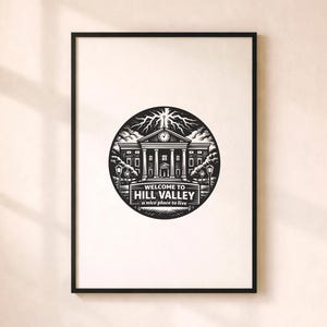 Puede incluir: Impresión enmarcada en negro con un diseño circular que muestra "WELCOME TO HILL VALLEY" y "a nice place to live". El diseño representa un juzgado, árboles y farolas sobre un fondo blanco.