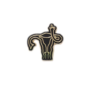 May include: Black enamel pin with a gold outline of a uterus with a middle finger raised in the air.