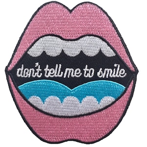 May include: Pink lips with a blue tongue and white teeth. The mouth is open and says "don't tell me to smile".