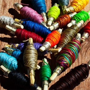 May include: A collection of colorful spools of thread, each wound around a wooden dowel. The spools are arranged in a random pattern, showcasing a variety of colors, including red, blue, green, orange, and yellow.