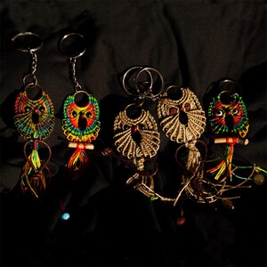 Puede incluir: Una colección de llaveros de búho de macramé hechos a mano. Los búhos presentan intrincados diseños tejidos en varios colores, incluyendo rojo, amarillo, verde y azul. Cada llavero tiene un anillo de metal y una borla decorativa.
