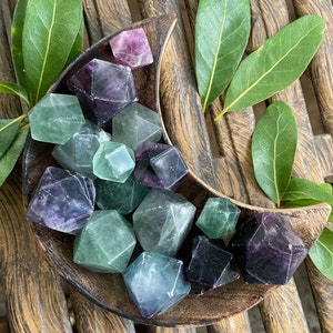 May include: A collection of green, purple, and blue fluorite crystals in various shapes and sizes. The crystals are arranged in a crescent-shaped wooden bowl.