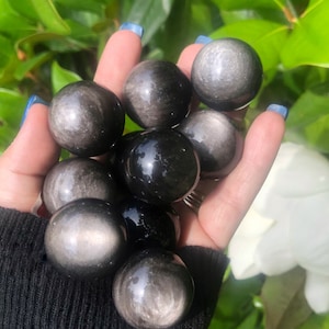 May include: A collection of black obsidian spheres with a silvery sheen. The spheres are smooth and polished, and they are arranged in a hand.