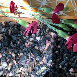 May include: A close-up of black and pink gemstones scattered on a wooden surface. Pink flowers are arranged on top of the gemstones.