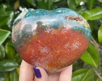 May include: A heart-shaped polished stone with red, green, and brown colors. The stone has a natural, rough texture.
