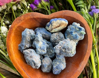 May include: A wooden heart-shaped bowl filled with rough, blue-green azurite stones. The bowl is surrounded by flowers.