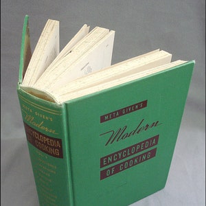May include: A green hardcover cookbook titled "Meta Given's Modern Encyclopedia of Cooking, Vol. 1." The book is open to a page with a recipe for freezing.