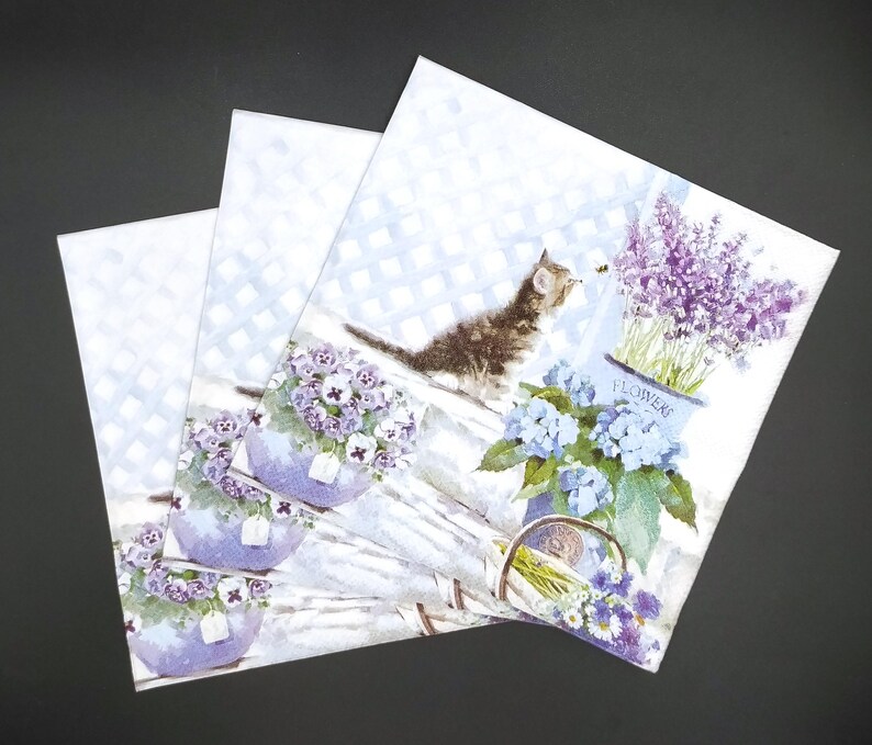 May include: Three white paper napkins with a floral and cat design. The napkins feature a cat looking at a bee, lavender flowers in a pot labeled "Flowers", and purple flowers in pots.