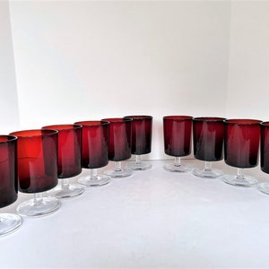 May include: Set of twelve red wine glasses with clear stems and bases. The glasses are made of glass and have a deep red color.