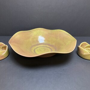 May include: A set of three ceramic bowls in a green and brown glaze. The large bowl is a shallow, wide bowl with a wavy edge. The two smaller bowls are round and have a flower-like shape.