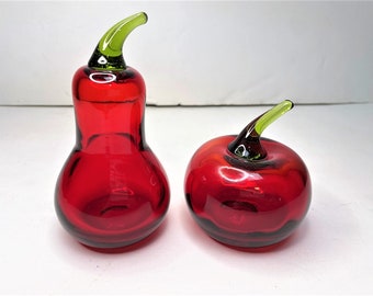 May include: Two red glass fruit sculptures, one shaped like a pear and the other like an apple, with green glass stems.