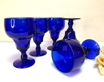 May include: Set of five cobalt blue glass goblets with a stemmed base. The goblets are all the same size and shape, and they have a clear, smooth surface.