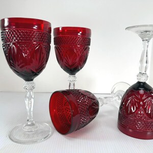 May include: Three ruby red glass goblets featuring a clear glass stem and base. The bowls of the glasses are decorated with a textured diamond pattern on the upper portion and a series of embossed leaf-like shapes around the lower section.