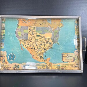 May include: Rectangular serving tray with a vintage map of North America under glass. The map is in shades of blue, yellow, and green, with state names and illustrations. The tray has a silver metal frame and handles.