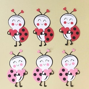 May include: Six paper cutouts of ladybugs holding hearts. The ladybugs are red with black spots and have white faces with pink cheeks. The hearts are pink and white.