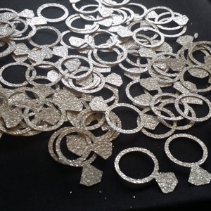 May include: A large pile of silver glitter engagement ring confetti. The rings are cut out of paper and have a sparkly finish.