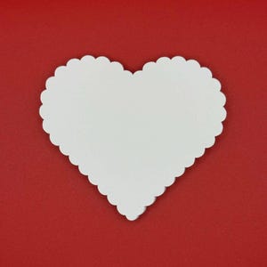May include: A white heart-shaped item with a scalloped edge, set against a solid red background. The heart is centered and takes up a significant portion of the frame, creating a simple, yet striking visual.