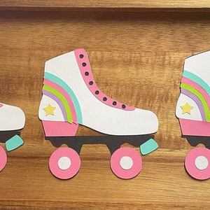 May include: Three white roller skates with pink wheels and rainbow accents. Each skate has a yellow star on the side.