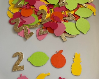 May include: A pile of colorful paper cutouts of fruit and the number two, with gold glitter. The fruit includes pineapples, lemons, bananas, cherries, and strawberries.
