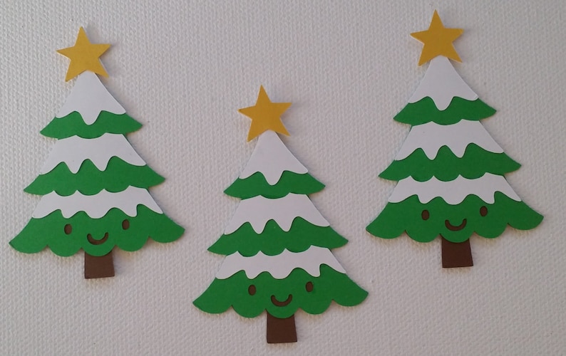May include: Three green paper Christmas trees with white snow accents and a yellow star on top. Each tree has a brown trunk and a smiling face.