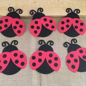 May include: Six red and black ladybug cutouts with black antennae and white spots. The ladybugs are made of paper and are approximately 3 inches in diameter.