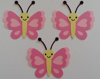 May include: Three pink paper butterflies with yellow centers and black antennae. Each butterfly has a smiling face.