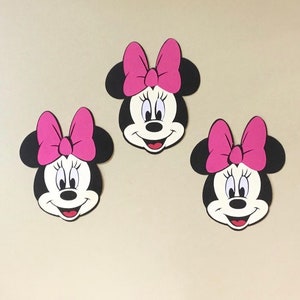 May include: Three black and white Minnie Mouse character cutouts with pink bows. The cutouts are on a light beige background.