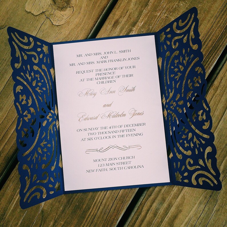 May include: A navy blue laser-cut gatefold wedding invitation with intricate floral patterns on the side panels. The white center insert features black printed text announcing the marriage of Mary Ann Smith and Edward Malcolm Jones on December 4th.