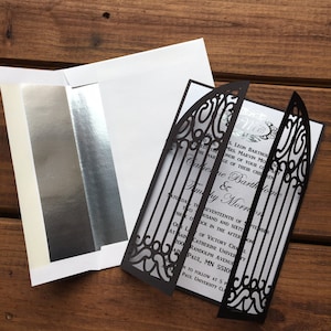 May include: A black and white wedding invitation with a laser-cut design of a gate. The text on the invitation reads "Saturday, the Seventeenth of September, Two Thousand and Sixteen, Three O'Clock in the Afternoon, Our Lady of Victory Chapel, at Saint Catherine University, 200 Randolph Avenue, Saint Paul, MN 55105, Reception to follow at 5 PM, Saint Paul University Club."