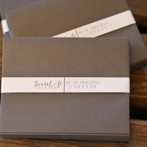 May include: A stack of 80lb gray envelopes with a white label that reads "Laurel St Design 80 LB ENVELOPES 4 3/8 X 5 3/4"