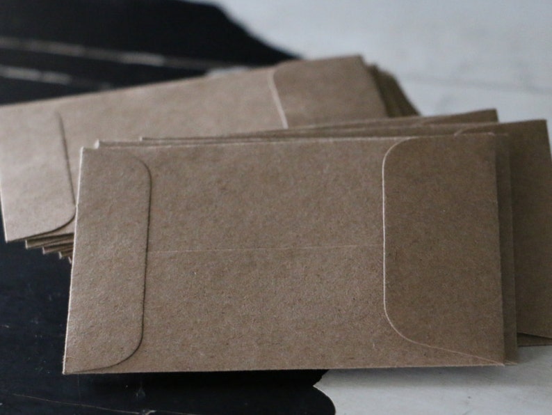 May include: A stack of brown kraft paper envelopes with a flap on the top. The envelopes are blank and ready to be addressed.