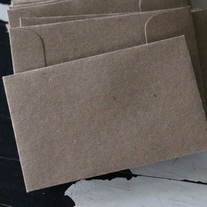 May include: A stack of brown paper envelopes with a flap on the top. The envelopes are made of a textured paper.