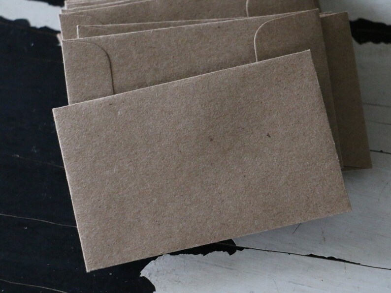 May include: A stack of brown paper envelopes with a flap on the top. The envelopes are made of a textured paper.