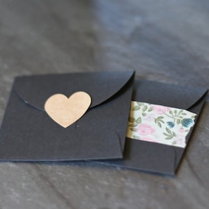 May include: Two black envelopes, one with a brown heart-shaped sticker and the other with a floral patterned tape.