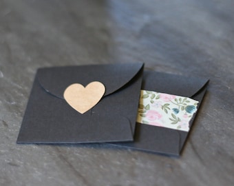 May include: Two black envelopes, one with a brown heart-shaped sticker and the other with a floral patterned tape.