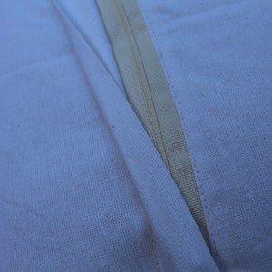May include: Close-up of a white fabric seam with a zipper running down the center.