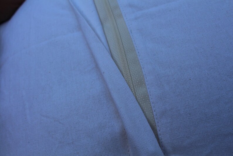 May include: Close-up of a white fabric seam with a zipper running down the center.