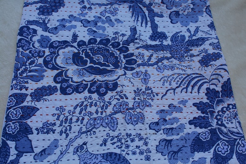 May include: Blue and white kantha quilt fabric with a floral and bird pattern. The fabric is quilted with a running stitch in a light blue thread.