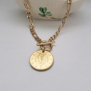 May include: A gold chain necklace with a toggle clasp and a gold coin pendant featuring the Irish harp and the year 2010.