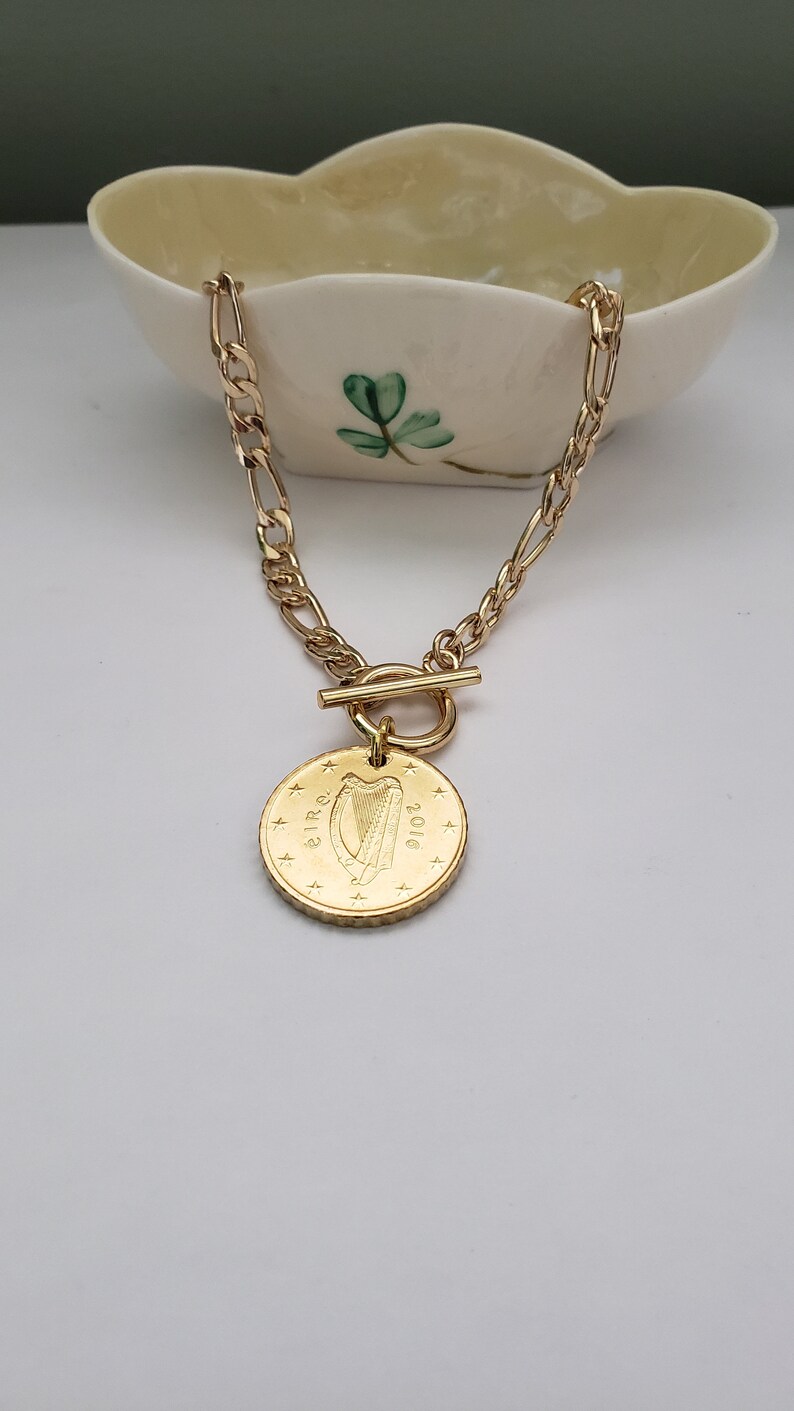 May include: A gold chain necklace with a toggle clasp and a gold coin pendant featuring the Irish harp and the year 2010.