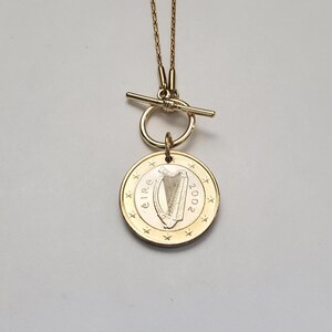May include: A gold necklace with a toggle clasp and a pendant featuring a 2002 Irish euro coin with a harp design. The coin has the word "&Eacute;IRE" and the year "2002" inscribed on it.