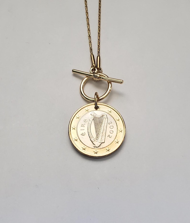 May include: A gold necklace with a toggle clasp and a pendant featuring a 2002 Irish euro coin with a harp design. The coin has the word "&Eacute;IRE" and the year "2002" inscribed on it.