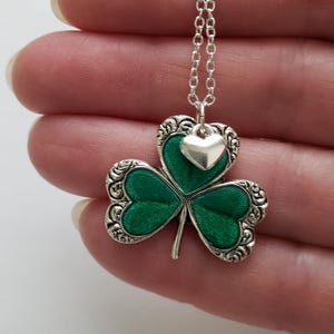 May include: A silver chain necklace with a green shamrock pendant and a small silver heart charm.