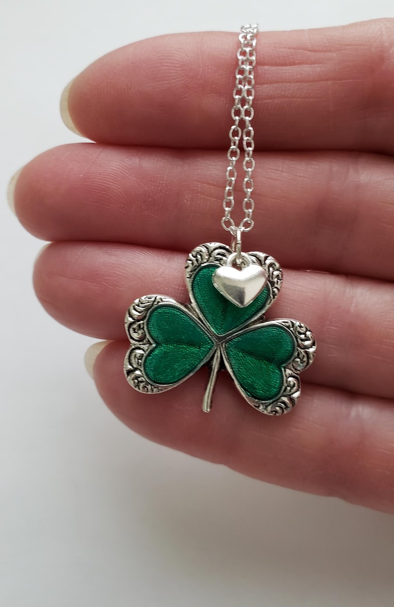 May include: A silver chain necklace with a green shamrock pendant and a small silver heart charm.