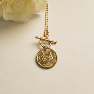 May include: Gold necklace with a toggle clasp and a Singapore dollar coin pendant. The coin features the Singapore coat of arms and the year 1995.