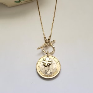 May include: Gold necklace with a toggle clasp and a pendant featuring a 2002 Irish euro coin with a shamrock charm.