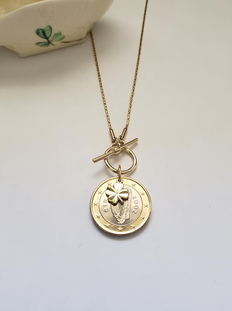 May include: Gold necklace with a toggle clasp and a pendant featuring a 2002 Irish euro coin with a shamrock charm.