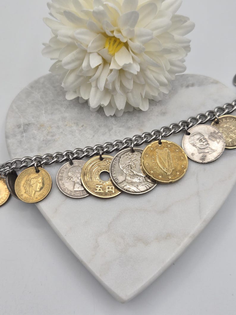 Pode incluir: Uma pulseira de corrente de metal prateado com uma cole&ccedil;&atilde;o de v&aacute;rias moedas internacionais como berloques. As moedas incluem pe&ccedil;as douradas e prateadas com diversos retratos, s&iacute;mbolos e textos, incluindo uma moeda japonesa de cinco ienes.