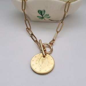 May include: A gold chain necklace with a gold coin pendant featuring the Irish harp and the word "EIR" and the year "2016".